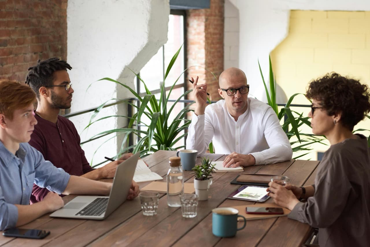 Team of 3 men and 1 woman sitting down in the loft of a modern office space having a discussion