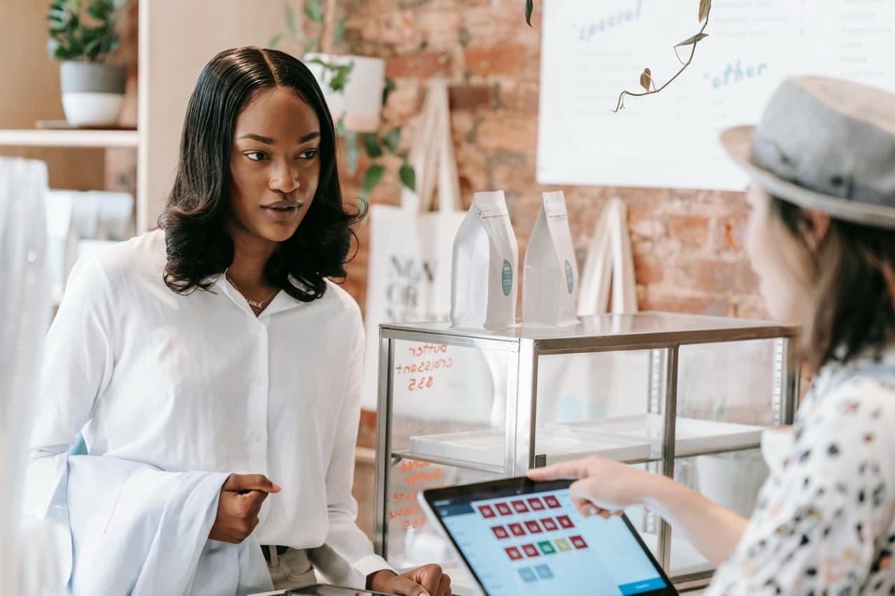 A female customer stands in front of a checkout counter at a retail store being serviced on a tablet by the clerk